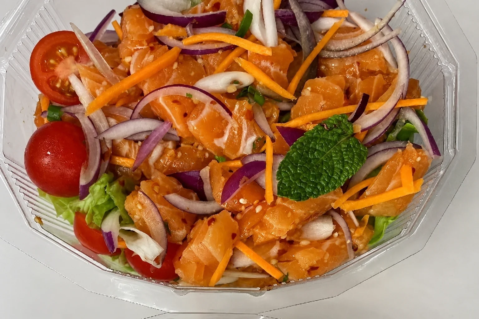 Salade de saumons à la citronnelle dans une boîte transparente sur un fond clair
